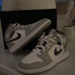 Nike Air Jordan 1 Mid, smoke grey/white anthracite - Air Jordan 1 Mid – Stil och komfort i perfekt balans!  Uppgradera din sneakerkollektion med dessa stilrena Air Jordan 1 Mid i en elegant färgkombination av vitt, grått och svart. Den ikoniska silhuetten erbjuder en tidlös design med hög komfort, perfekt för både vardagsbruk och streetwear-outfits.  Skorna är knappt använda och använda ett fåtal gånger!