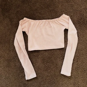 Beige ribbad offshoulder topp - Säljer en snygg beige ribbad offshoulder topp med långa ärmar. Toppen är croppad och perfekt för en trendig look. Passar utmärkt till jeans eller kjol för en stilren outfit.