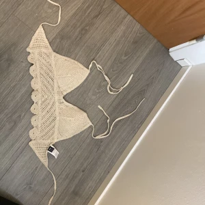 Beige stickad bikiniöverdel - Snygg beige stickad bikiniöverdel med knytband och volangdetaljer. Perfekt för en somrig dag på stranden. Den har en triangelformad design och ger en bohemisk känsla.