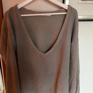 Beige stickad tröja från NA-KD - Säljer en mysig beige stickad tröja från NA-KD med djup v-ringning. Perfekt för kyliga dagar med sin långa ärmar och mjuka material. En stilren och bekväm tröja för alla tillfällen.