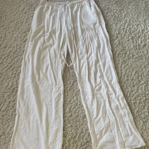 Vita linnebyxor från Divided - Säljer ett par vita linnebyxor från Divided. Byxorna har en loose passform med elastisk midja och snörning för extra komfort. Perfekta för varma dagar med sitt lätta och luftiga material.