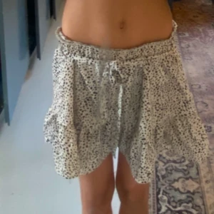 Vit kortkjol med volang - Söt kortkjol med svart prickigt mönster på vit bakgrund. Kjolen har en volangdetalj och knytband i midjan.  Perfekt för en sommar dag. Mycket var skick och nästan inte använd. Inga hål. Inga fläckar 