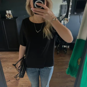 Svart topp med öppen rygg - Snygg svart topp med korta ärmar och en stilren design. Toppen har en unik detalj med öppen rygg som ger en extra touch. Perfekt för en chic och avslappnad look.