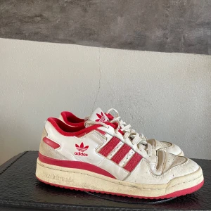 Adidas Forum low - Snygga Adidas sneakers i vitt med röda detaljer och den klassiska tre-randiga designen. Skorna har snörning och en röd yttersula med ett unikt mönster. Storleken i skorna är 42 2/3. Priset är inte hugget i sten!