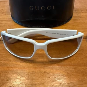 Vita solglasögon från Gucci - Snygga vita solglasögon från Gucci med en modern design. De har en rektangulär form och märkeslogga på sidan. Perfekta för att ge din stil en lyxig touch.