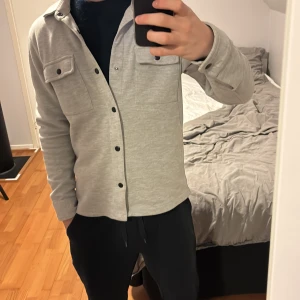 Grå overshirt med knappar selected homme  - Säljer en stilren grå overshirt med knappar och två bröstfickor. Perfekt för lager-på-lager och passar till många olika outfits. Skjortan har långa ärmar och en klassisk krage. Används sparsamt och köpt för typ en månad sedan. Hör av er vid frågor. Priset är definitivt inte hugget i sten😇