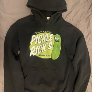 Svart hoodie med Pickle Rick motiv - Säljer en svart hoodie med ett coolt Pickle Rick tryck från Rick and Morty. Perfekt för fans av serien! Hoodien har en klassisk passform med en stor ficka framtill och en bekväm huva. Prisförslag går att lägga 