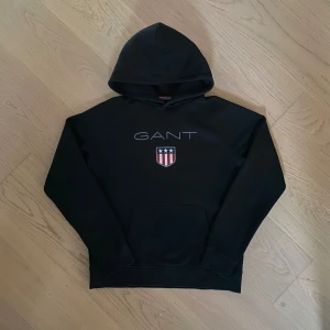 GANT hoodie - Riktigt snygg GANT hoodie i nyskick. Hoodien är i svart med ett stilrent tryck på framsidan. Skriv för mer bilder eller funderingar!🙌