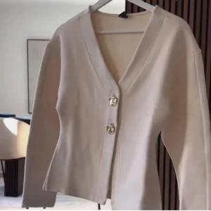 Begie cardigan ifrån gina - Snygg vit kofta från gina med v-ringning och dekorativa knappar framtill. Perfekt för en stilren look. Passar bra till både jeans och kjol.