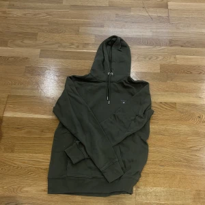 Grön hoodie från Gant - Säljer en stilren grön hoodie från Gant med justerbar huva och ribbade muddar. Perfekt för en avslappnad look. 💚