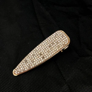 Glittrig hårklämma i guld - Snygg och elegant hårklämma i guld med glittrande stenar. Perfekt för att ge en extra touch till din frisyr. Klämman har en avsmalnande form och är lätt att använda.