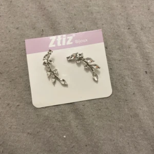 Silvriga örhängen från Ztiz Bijoux - Eleganta silvriga örhängen från Ztiz Bijoux med ett bladliknande mönster. Perfekta för att ge en stilren touch till din outfit. De har en glittrig finish som fångar ljuset vackert.