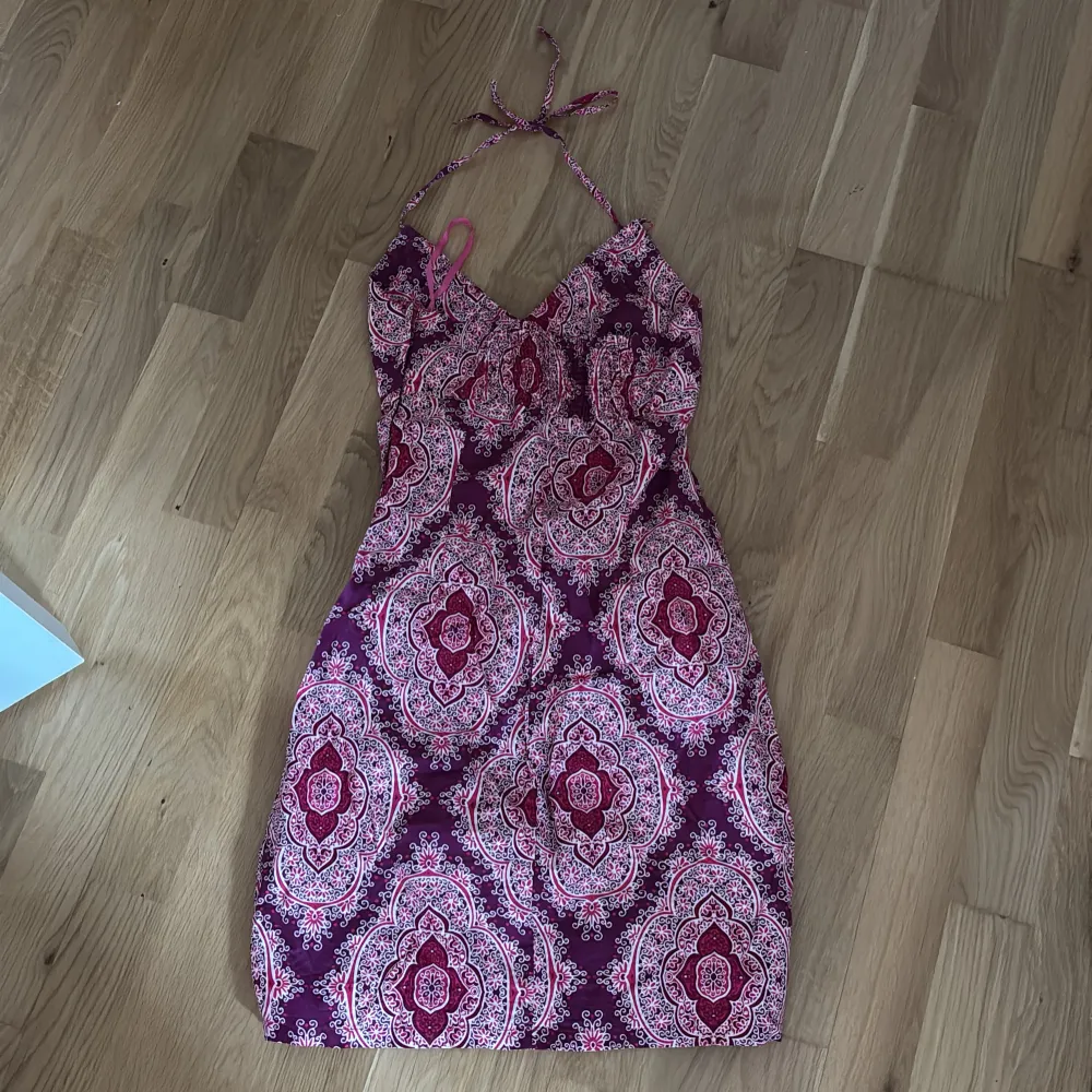 Säljer en snygg mönstrad klänning från H&M i mörkare rosa och rosa. Klänningen har en omlott-design med knytband runt halsen och ett vackert mönster. Perfekt för sommarens alla tillfällen!. Mekot.
