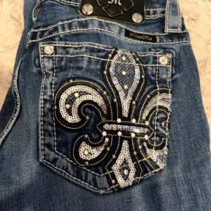 Blå jeans från Miss Me - Snygga blå skinny jeans från Miss Me med en cool broderad bakficka dekorerad med paljetter. Jeansen har en låg midja och är tillverkade i en bomullsblandning med lite stretch för extra komfort.