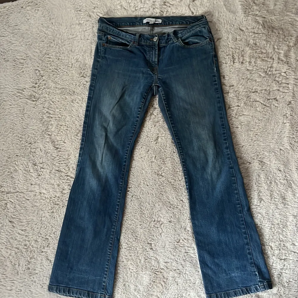 Säljer ett par klassiska blå jeans från Lindex. De har en blandning mellan rak och bootcut passform med femficksdesign och knappgylf. Perfekta för en avslappnad stil. Jeansen har tyvärr ett hål på båda sidorna som syns på sista bilden men går super enkelt att fixa med lite nål och tråd! Original priset ligger mellan 400-700kr.. Farkut & Housut.