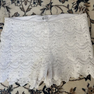 Vita spets shorts - Säljer ett par vita shorts med vacker spetsdesign. De har en elegant och feminin look med fina detaljer. Perfekta för sommarens varma dagar.