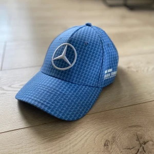 Blå keps från Mercedes AMG Petronas - Snygg blå keps med rutigt mönster och Mercedes-logga framtill. Kepsen har justerbar passform och broderade detaljer. Perfekt för racingfans!