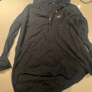 Svart blus från Hollister - Säljer en svart blus/skjorta från Hollister med knappar vid ärmslutet. Skjortan har en klassisk krage. 