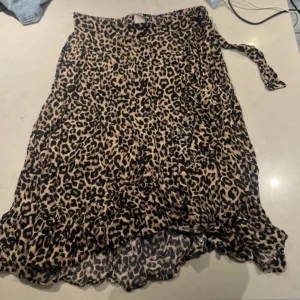 Leopardmönstrad kjol från Lindex - Snygg leopardmönstrad kjol från Lindex i storlek 146/152. Kjolen har ett omlottutseende med volangdetaljer och ett knytband i sidan. Jättestretchig. Passar s/m