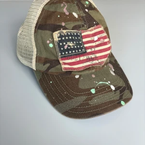 Denim & supply Ralph Lauren keps - Snygg keps i camouflage-mönster med en patch av den amerikanska flaggan framtill. Kepsen har en beige mesh-baksida för ventilation och en cool, stänkmålad design i olika färger. Perfekt för en avslappnad stil. Kepsen är från Denim & supply Ralph Lauren. Väldigt unik och snygg. Den är snapback så man ställer in storlek själv. Vet inte kepsstorleken.