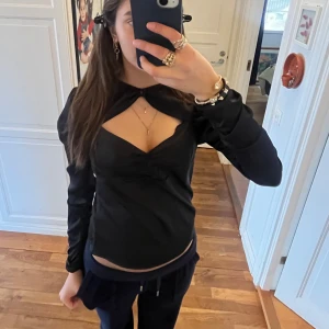 Svart långärmad topp med öppen detalj - Snygg svart långärmad topp med en unik öppen detalj framtill. Perfekt för att ge en stilren och modern look. Passar bra till både jeans och kjol.