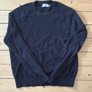 Svart stickad tröja från East West - Säljer en stilren svart stickad tröja från East West. Tröjan har en rund halsringning och långa ärmar, perfekt för kyligare dagar. Den ribbade strukturen ger en klassisk look.  Det är storlek L men sitter som M. För mer information kom PM.