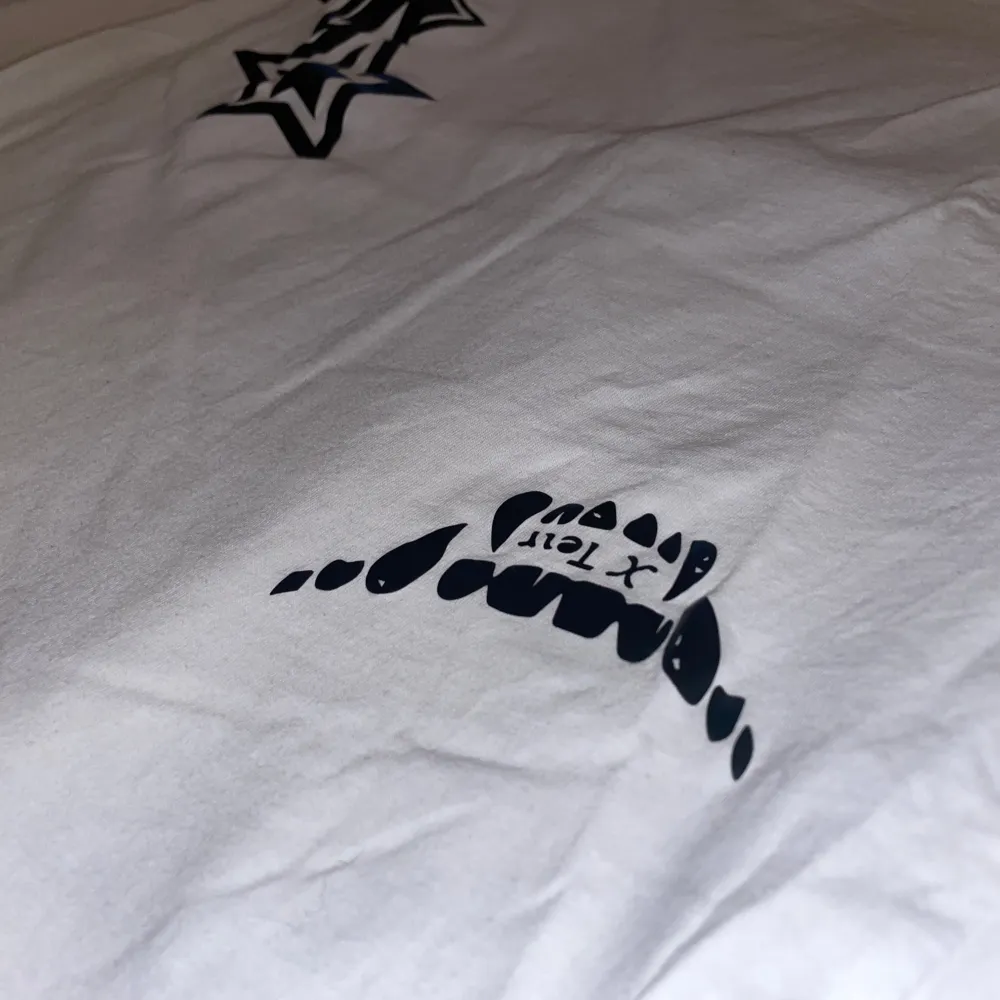 Cool vit t-shirt med tryck av svarta stjärnor på framsidan och en stor åtta-boll på baksidan. Perfekt för en avslappnad stil med en twist. Passar bra till jeans eller shorts för en casual look.. T-paidat.