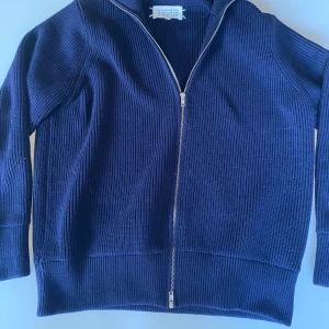 Maison margiela zip - Säljer en stilren mörkblå ribbad tröja från Maison Margiela. Tröjan har en praktisk dragkedja framtill och långa ärmar. Perfekt för en avslappnad men ändå elegant look. Passar bra till både jeans och chinos.