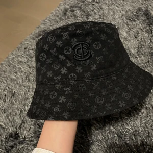 NY Svart mönstrad denim bucket hat - Snygg svart bucket hat med diskret mönster och broderad text. Perfekt för att ge din outfit en cool touch. Passar både till vardag och speciella tillfällen.