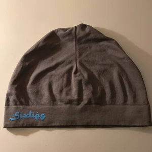 Grå mössa från Sixties - Snygg grå mössa från Sixties med en stilren design. Mössan har en diskret blå logga på framsidan och är tillverkad i ett mjukt material som passar perfekt för kyligare dagar.