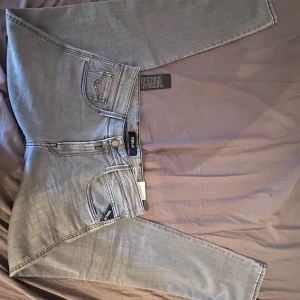 Grå jeans från Replay - Snygga grå jeans från Replay i modellen Anbass. De har en klassisk femficksdesign med dragkedja och knapp. Perfekta för en stilren look. Storlek W30 L34, Aldrig använda pågrund av fel storlek