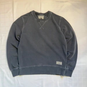 Grå/blå sweatshirt från Marc O'Polo - Säljer en stilren grå sweatshirt från Marc O'Polo med vintage-stil. Tröjan har långa ärmar och ett broderat märke på framsidan. Perfekt för en avslappnad look. 🩶