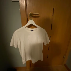 Vit t-shirt från Polo Ralph Lauren - Säljer en klassisk vit t-shirt från Polo Ralph Lauren med det ikoniska broderade logotypen på bröstet. T-shirten är kortärmad och tillverkad i mjuk bomull. Perfekt för en stilren och avslappnad look.