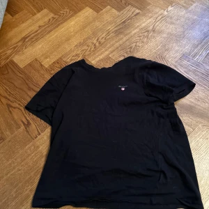 Svart t-shirt från Gant  - Säljer en klassisk svart t-shirt från Calvin Klein. Den har en enkel design med korta ärmar och en liten logga på bröstet. Perfekt för en stilren look.