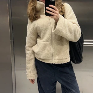 Beige teddyjacka från HM - Mysig beige teddyjacka med dragkedja framtill och långa ärmar. Perfekt för kyligare dagar med sin fluffiga och varma design. Jackan har en enkel och stilren look som passar till många olika outfits.