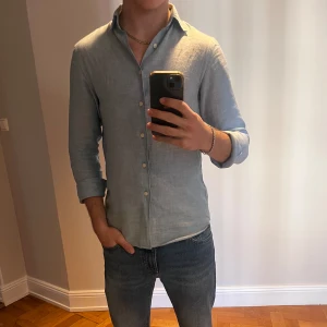 Ljusblå linneskjorta - Säljer en stilren ljusblå linneskjorta från Uniqlo i storlek XS. Skjortan har långa ärmar och knappar framtill, perfekt för en avslappnad men ändå uppklädd look. Hör av dig vid minsta fråga eller fundering!