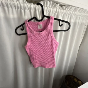 Rosa ribbad linnetopp - Säljer en söt rosa ribbad linnetopp. Perfekt för sommardagar och kan enkelt matchas med jeans eller kjol. Toppen är ärmlös och croppad för en trendig look.