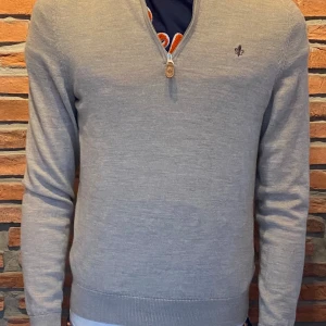 Grå merinoulltröja från Morris - Säljer en stilren grå tröja från Morris i 100% merinoull. Tröjan har en dragkedja vid halsen och ett diskret emblem på bröstet. Perfekt för kyligare dagar. Pris går att diskutera vid snabb affär!