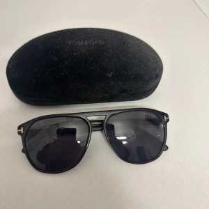 Tom Ford solglasögon  - Snygga svarta solglasögon från Tom Ford med en klassisk design. De har en elegant svart båge och mörka linser. Perfekta för att ge en stilren look.
