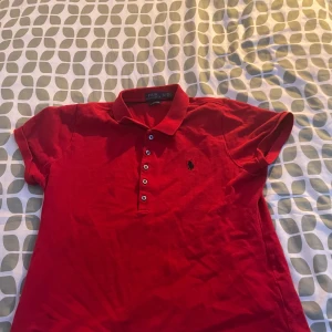 Röd pikétröja från Ralph Lauren - Säljer en snygg röd pikétröja från Ralph Lauren. Tröjan har en klassisk krage och knappar framtill. Perfekt för en stilren look. 🏷️