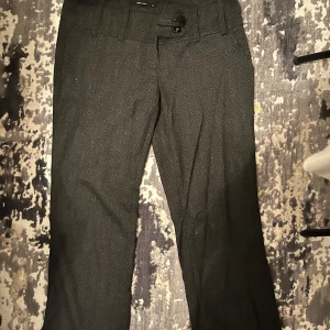 Grå kostymbyxor från Vero Moda - Snygga grå Lågmidjade  kostymbyxor från Vero Moda med en klassisk design. Byxorna har en rak passform och är perfekta för en stilren look. De har knappar och hällor för bälte i midjan. Passar mig som bär storlek 36.