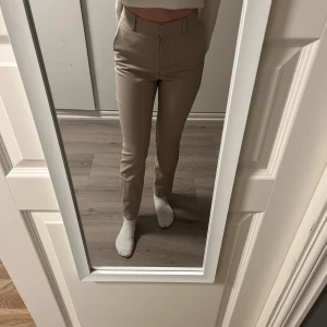 Beige kostymbyxor - Snygga beige kostymbyxor med hög midja och rak passform. Byxorna har en stilren design med bälteshällor och diskreta fickor baktill. Bra skick förutom defekten mellan benen (sista bilden) men går nog att fixa för den som kan sy!