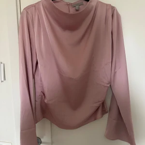 Rosa långärmad blus från H&M - Elegant rosa blus från H&M i ett mjukt och glansigt material. Blusen har långa ärmar och en diskret dragkedja i ryggen för en smidig passform.