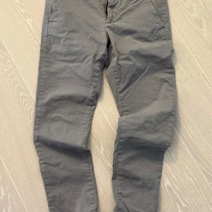 Grå chinos från Dondup - - Snygga grå chinos från Dondup med en klassisk design. Byxorna har en normal passform och är tillverkade i bomull, vilket gör dem bekväma och stilrena. Perfekta för en avslappnad men ändå uppklädd look.