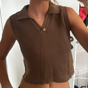 Brun stickad topp Brandy Melville - Säljer en brun stickad topp från Brandy Melville. Toppen är ärmlös, croppad och har en snygg krage med v-ringning.