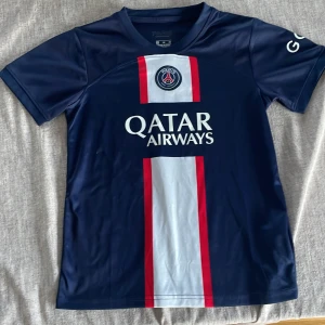 PSG Neymar Jr #10 matchställ - Säljer ett PSG matchställ med Neymar Jr #10. Tröjan är marinblå med röd och vit rand i mitten, PSG-logga och Qatar Airways-tryck. Korta ärmar och sportigt material. Tillhörande shorts i marinblått med PSG-märke och nummer 10. Perfekt för fotbollsfans!(storlek 30) passar barn i 10-12 år 
