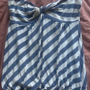 Randig tubtopp från World Wide Wear - Snygg tubtopp från World Wide Wear i blått och vitt med diagonala ränder. Toppen har twistad detalj framtill och elastisk nederkant för en bekväm passform. Perfekt för varma dagar och enkel att styla med jeans eller kjol.