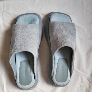 Grå/ Blå mockasandaler från Eytys - Chunky sandaler från Eytys i ljusgrå mocka med bred rem och fyrkantig tå. Sval design med kraftig, mönstrad sula och mjuk innersula för extra komfort. Perfekta för dig som gillar minimalistisk och modern stil. Större passform.