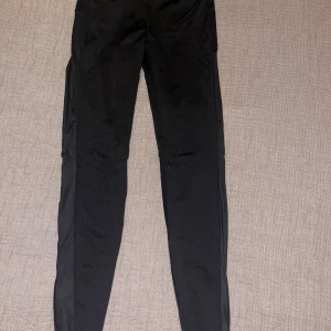 Svarta träningsleggings  - Svarta träningsleggings från H&M Sport med meshpaneler på benen och reflexdetaljer längst ner. Hög midja med justerbar snörning i midjan. Tillverkade i stretchigt syntetmaterial som andas, perfekta för löpning eller gym.