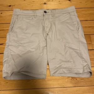 Beige shorts från Kappahl - Snygga beige shorts från Kappahl med klassisk passform och midwaist. De har två sidofickor, två bakfickor med knapp och bälteshällor. Perfekta för varma dagar och enkla att matcha med det mesta. Materialet är mjukt och skönt. 